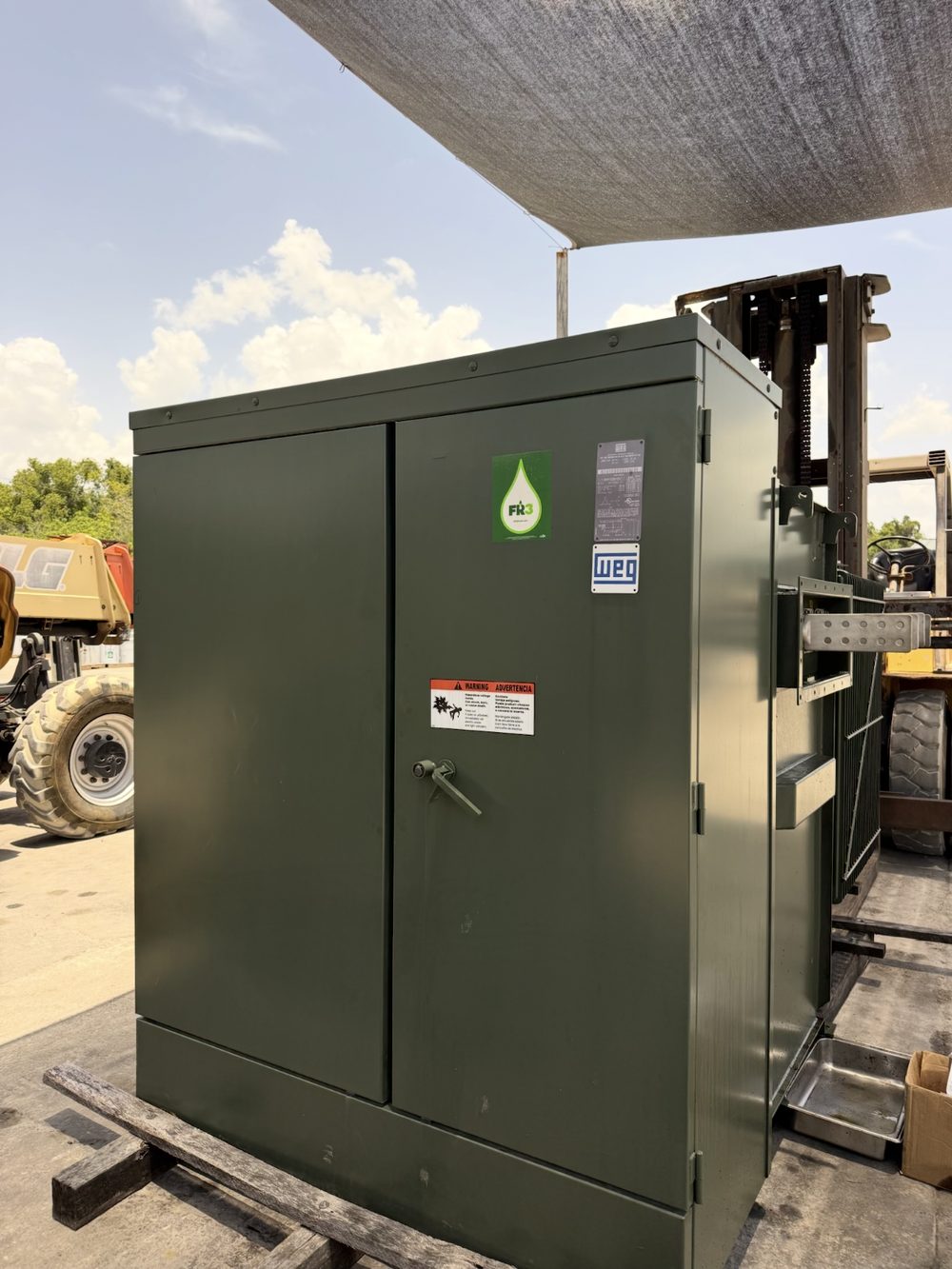 Used WEG pad-mount transformer with FR3 fluid and visible nameplate, staged on skids in the yard before pickup